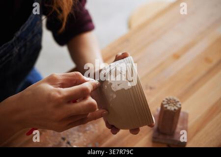 Hands of Vietnamese female potter holding and carving clay pot while sitting at table in studio Stock Photo