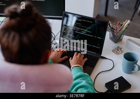 Woman typing codes on laptop sitting at table in office Stock Photo