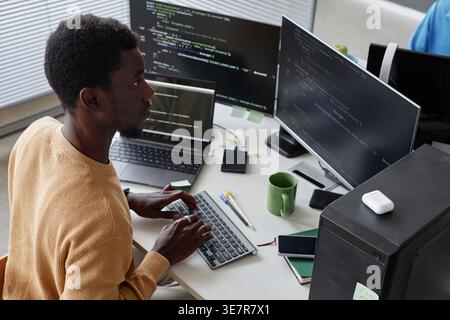Black male programmer typing codes on computer sitting at table with laptop in office Stock Photo