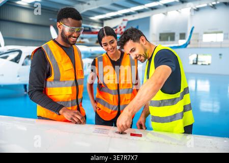 Diverse aircraft maintenance crews inspecting airplane wing in hangar Stock Photo