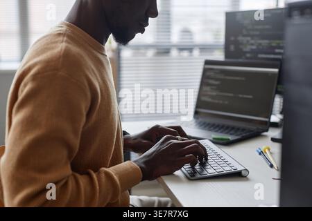 Black male programmer typing codes on computer sitting at table with laptop in office Stock Photo