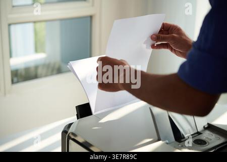 Hands of Mixed race man putting papers on printer to print documents in office Stock Photo
