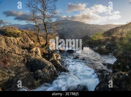 Sunlit water flows over rocks through a rugged landscape in Galloway Forest Park, Scotland. Stock Photo