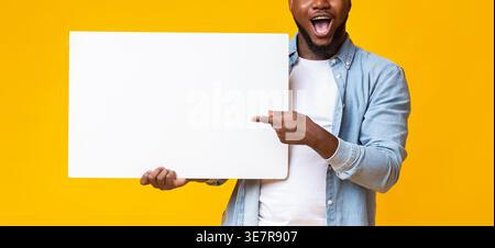 Black man pointing to blank whiteboard in his hands standing against yellow background in studio Stock Photo