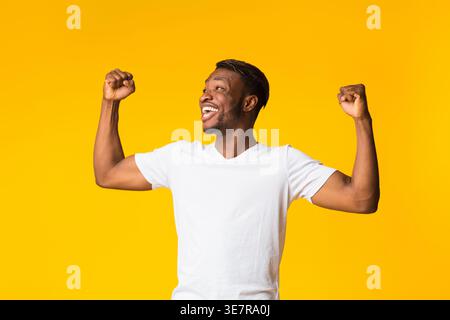 Yes. Excited Afro Guy Rejoicing Success Shouting And Shaking Fists Standing On Yellow Background. Studio Shot Stock Photo