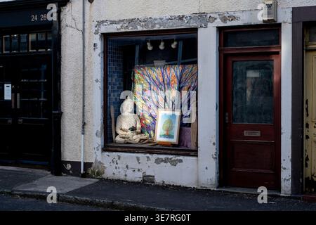 Weathered storefront window with a Buddha statue, colorful backdrop, and framed artwork creates a serene street scene. Stock Photo