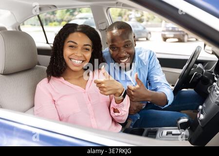 Smiling Black couple gesturing thumbs up while riding car together in city Stock Photo