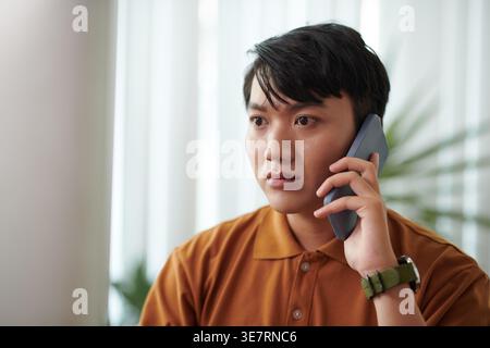 Worried Asian male having phone call standing at home Stock Photo