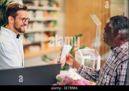 Senior Black male customer taking prescription medicine from pharmacist assistant at the counter standing inside pharmacy Stock Photo