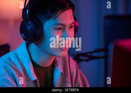 Asian man wearing headphones with microphone while playing video game on computer at home Stock Photo