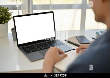 Asian businessman taking notes on notebook looking at laptop while sitting at table in office Stock Photo
