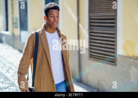Black male carrying bag walking on street on sunny day Stock Photo