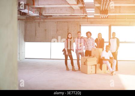 Group of diverse business people standing together with Black man sitting on cardboard boxes in empty unfinished office building Stock Photo