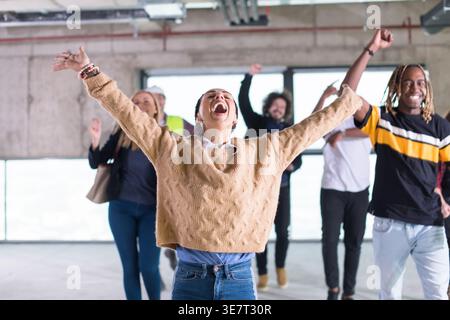 Cheerful Group of diverse business people raising arms looking away while dancing together in empty unfinished office building Stock Photo