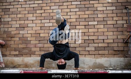 Asian male hiphop dancer in beanie doing headstand breakdancing on street during daytime Stock Photo