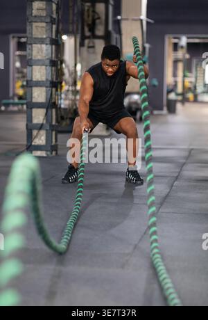 Muscular Black male working out using battle rope standing in gym during fitness training Stock Photo