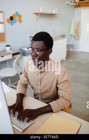 Black male IT specialist with eyeglasses working on computer while sitting at table in office Stock Photo