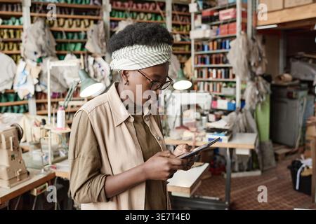 Black female designer wearing eyeglasses using tablet while standing in workshop Stock Photo