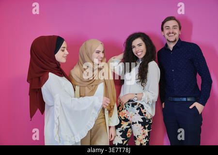 Middle Eastern women in traditional Muslim clothing standing with male and female friends against pink background in studio Stock Photo
