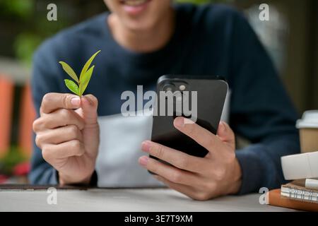 Cropped image of Asian man holding smartphone and a green leaves sitting at table in cafe Stock Photo