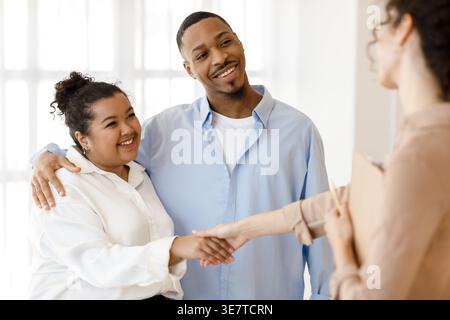 Smiling Black and Hispanic couple shaking hands with female psychologist while standing in clinic Stock Photo