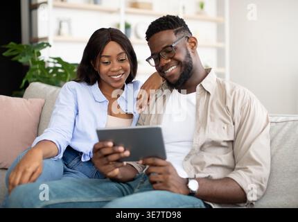 Black couple using tablet together sitting on sofa at home Stock Photo
