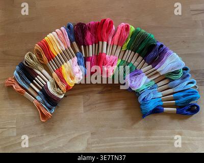 Vibrant rainbow of colorful embroidery floss skeins arranged in an arc on wood Stock Photo