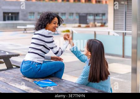Hispanic and Asian female students talking and holding hands while sitting at a study table in campus university during daytime Stock Photo