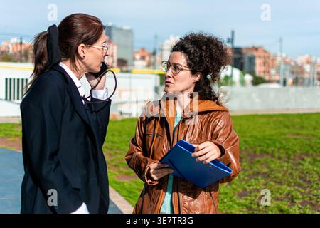 Businesswomen talking outdoors discussing project details Stock Photo