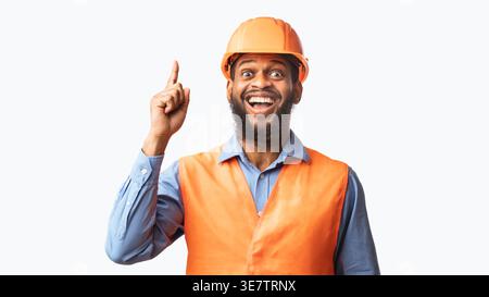 Black male worker wearing safety helmet pointing finger up while standing against white background in studio Stock Photo