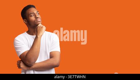 Black man wearing white shirt touching his chin looking away thinking against orange background Stock Photo