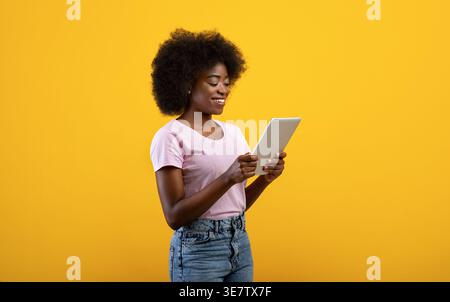 Black female with afro using tablet standing against yellow background in studio Stock Photo