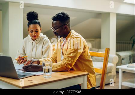 Black man and mixed-race woman discussing over document while sitting together at table at home Stock Photo