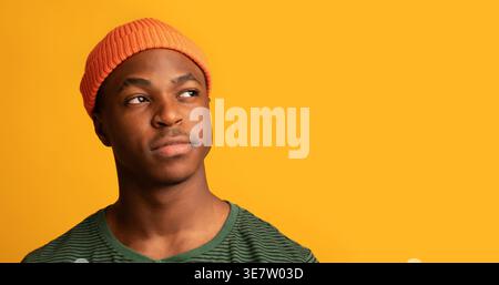 Black man in beanie looking away while standing against yellow background in studio Stock Photo
