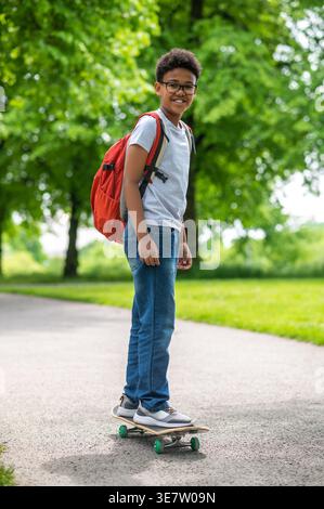 Black pre-teen boy wearing eyeglasses riding skateboard while in park Stock Photo