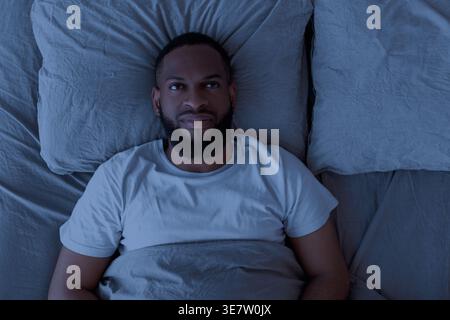 Black man suffering from insomnia looking up lying on bed at home Stock Photo