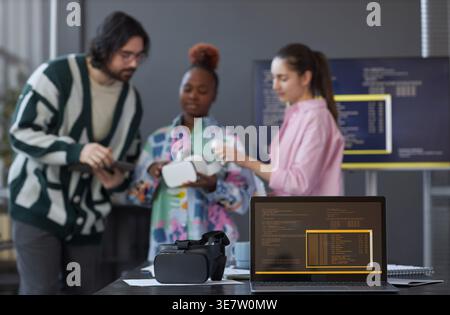 Group of diverse programmers discussing software and testing new VR glasses while standing together having a meeting in office Stock Photo
