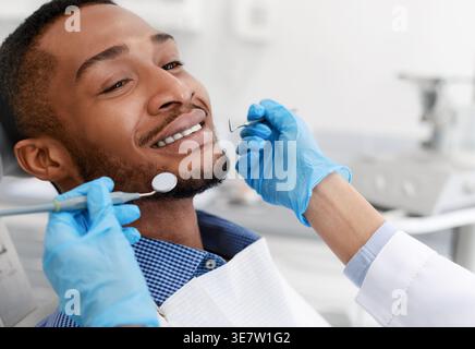 Black male patient getting his teeth checked by female dentist wearing gloves in clinic Stock Photo