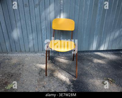 Empty yellow retro chair standing in front of a grey corrugated metal wall outdoors during a sunny day in the Czech Republic Stock Photo
