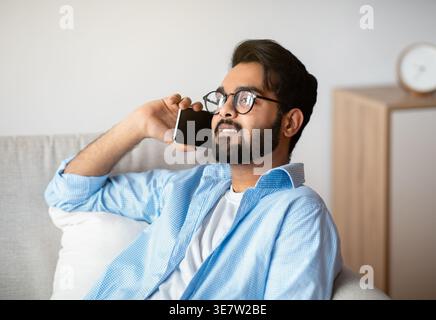 Relaxed Arab Man Talking On Celphone While Resting On Couch At Home In Living Room At Home, Millennial Eastern Guy In Eye Glasses Enjoying Pleasant Ph Stock Photo