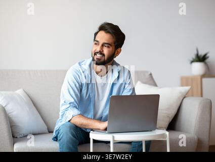 Portrait Of Pensive Arab Freelancer Guy Working With Laptop Computer At Home And Looking Aside, Thinking Thinking About Business Ideas, Thoughtful Eas Stock Photo