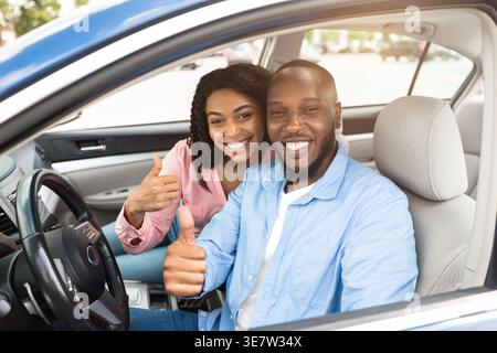 Smiling Black couple gesturing thumbs up while riding car together in city Stock Photo