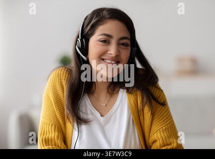 Smiling Middle Eastern woman wearing headsets sitting at home Stock Photo