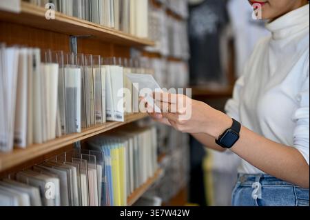 Asian female holding postcard standing near shelf in shop Stock Photo