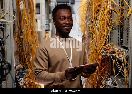 Black male system administrator holding tablet while standing in server room Stock Photo