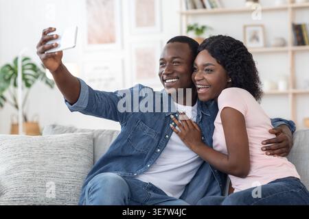 Black couple in love taking selfie on mobile phone while spending time together at home, free space Stock Photo