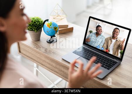 Black couple on laptop screen talking to caucasian female tour agent sitting at wooden table in office Stock Photo