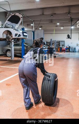 Chinese female mechanic pushing tire across the floor in auto repair shop Stock Photo