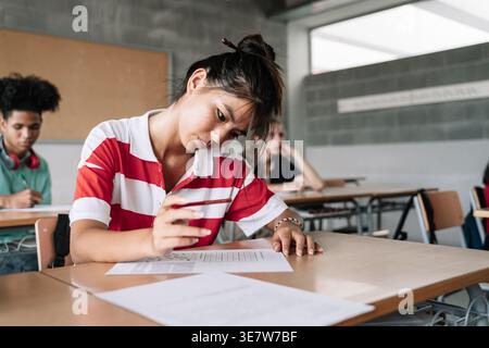 Asian female student and classmates sitting at desk taking exam in classroom Stock Photo