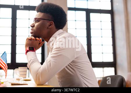 Black businessman leaning chin on hands sitting at table in office Stock Photo